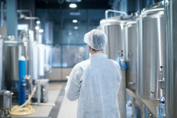 Technologist in white protective suit walking through food factory production line checking quality. Technologist in white protective suit walking through food factory production line checking quality.